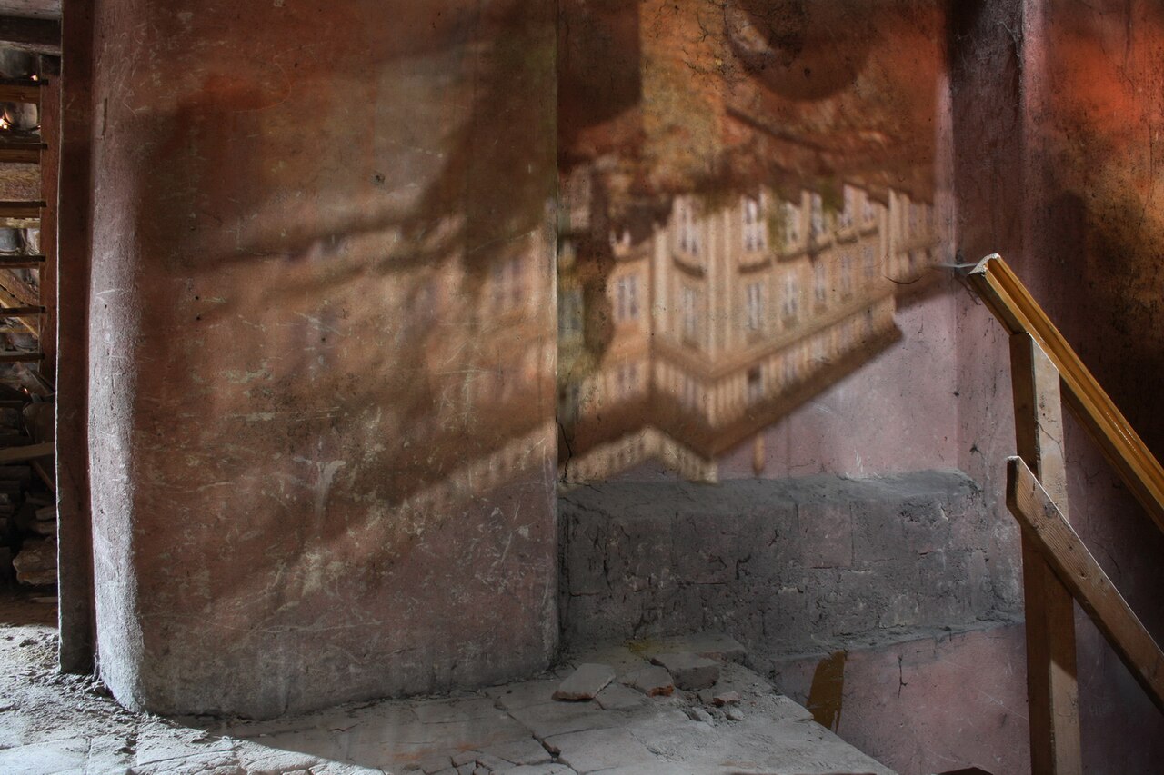 A large inverted image of Prague Castle's palace projected onto a dim attic wall by a single small hole in the tile roof.