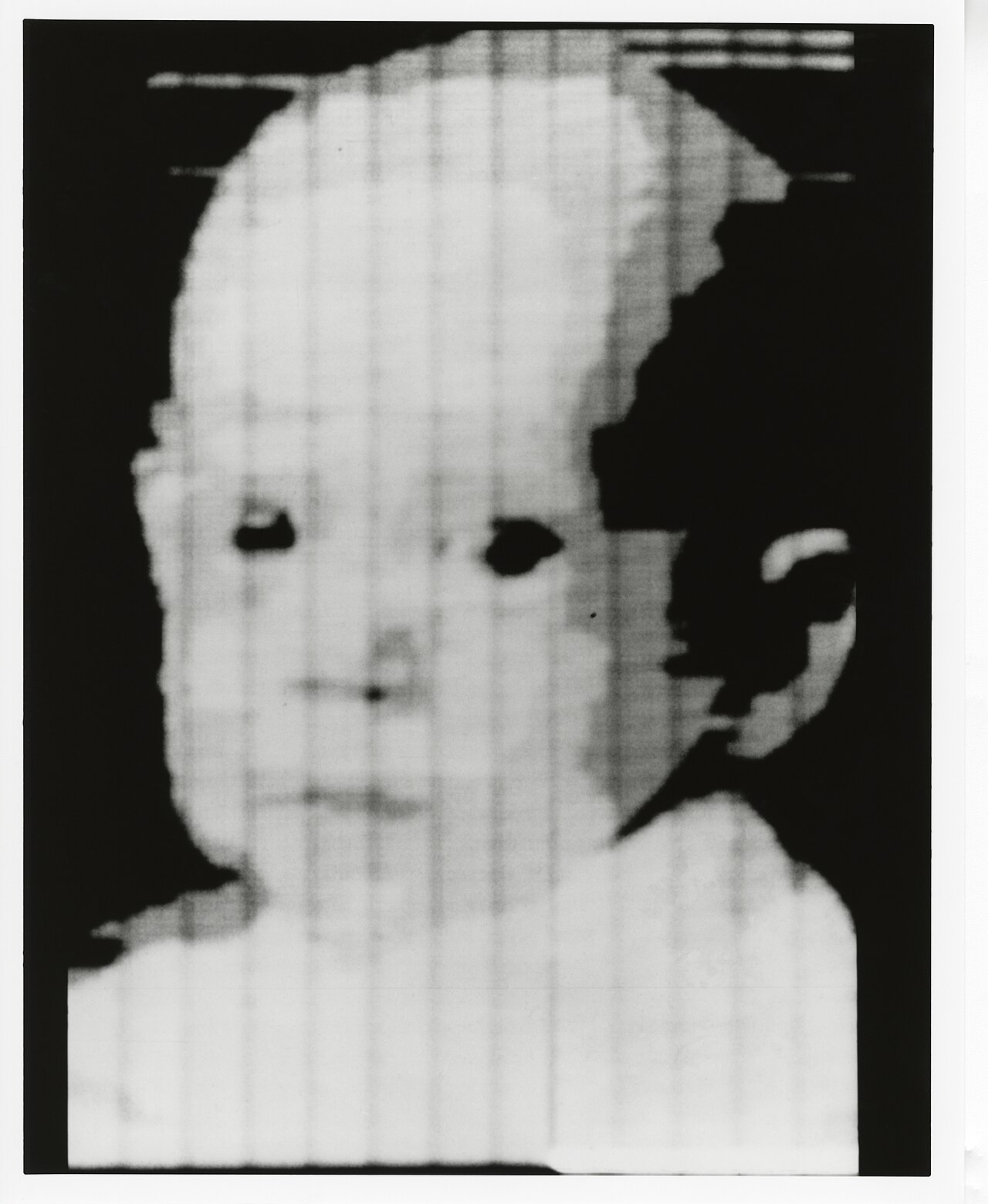 A grainy, low-resolution digital scan of an infant's face, the first photograph ever converted into pixels