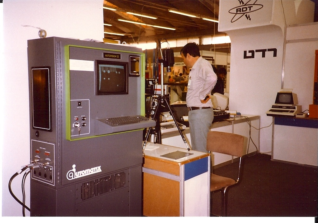 The Autovision II machine-vision system on display at a 1983 trade show, with a camera on a tripod over a light table and an image on a screen